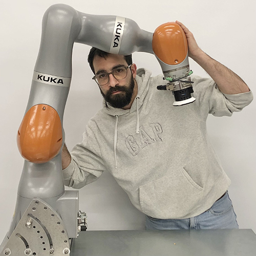 Photograph of Theodoros Stouraitis standing behind robot arm