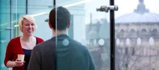 Two people chatting next to a glass wall, with McEwan Hall in the background