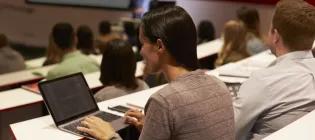 A woman in a lecture theatre with a laptop on the table