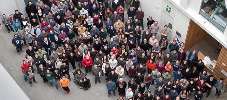 A large gathering of people standing on the ground floor of a modern building, looking up