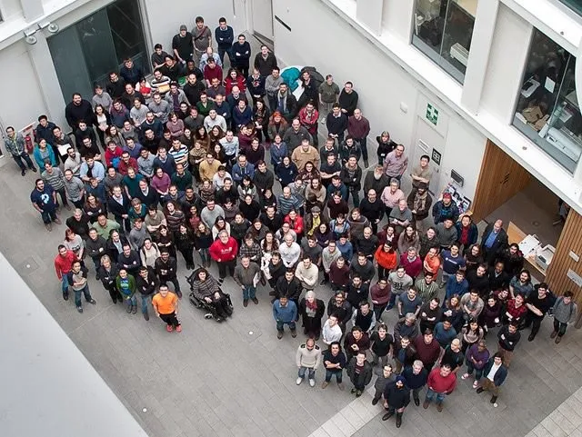 A large gathering of people standing on the ground floor of a modern building, looking up
