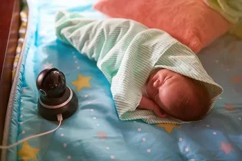 Wrapped up baby lying on a bad next to a baby monitor