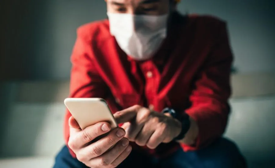 Photo of a man wearing a face mask typing on a mobile phone.