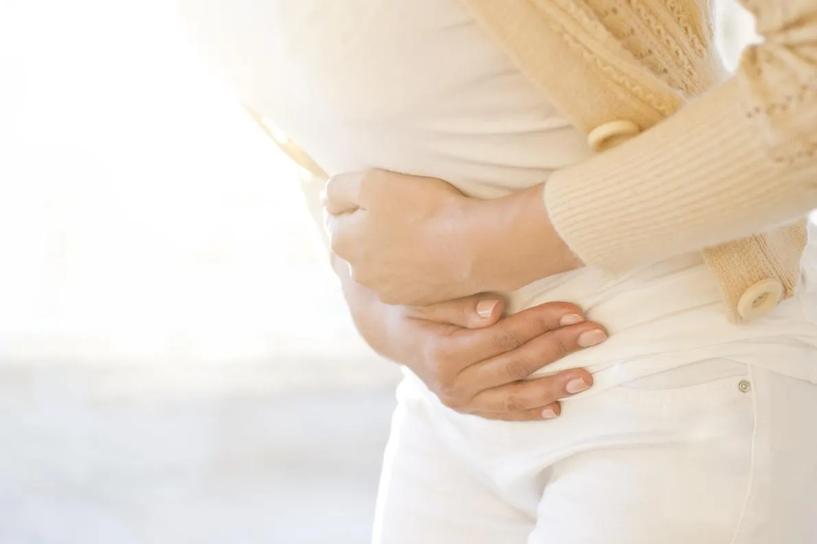 A photo of a woman's stomach from the side, her hands embracing it as if she was in pain