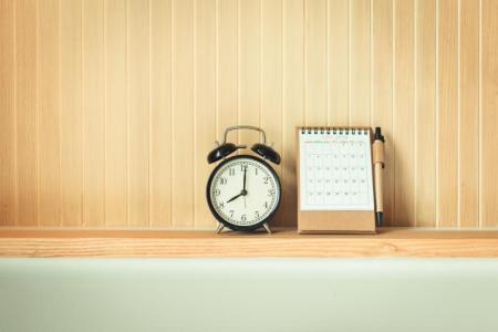 A photo of an analogue alarm clock on a shelf next to a paper desktop calendar