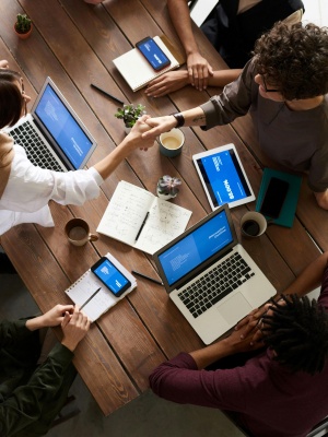 People around a table working on laptops with cups of coffee, two shaking hands across the table..